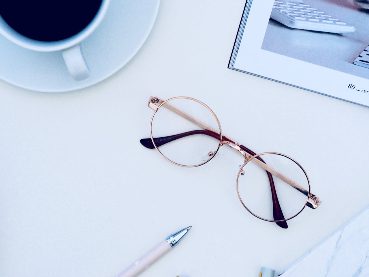 about-01 A clean, minimalist desk setup with a cup of coffee, eyeglasses, and a pen on a white surface.