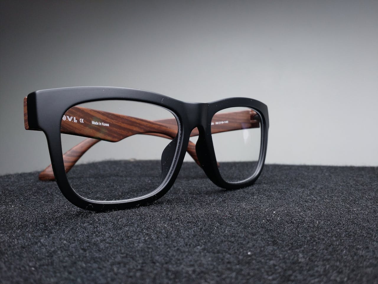 hero-img-01 Close-up of fashionable black and wooden frame glasses on dark fabric with a soft-focus background.