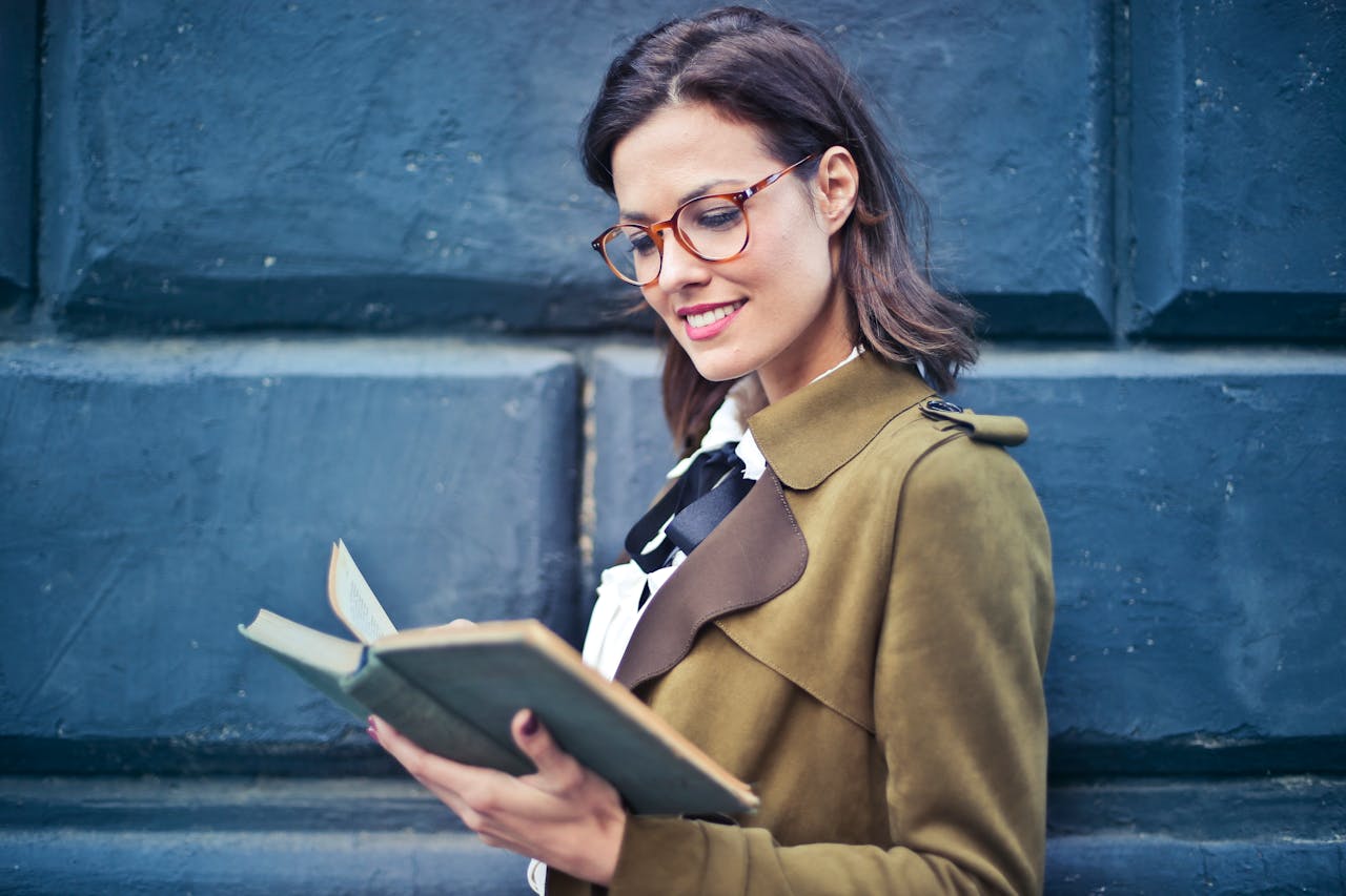 why-choose-us Smiling woman enjoying a book while standing against a textured blue wall.