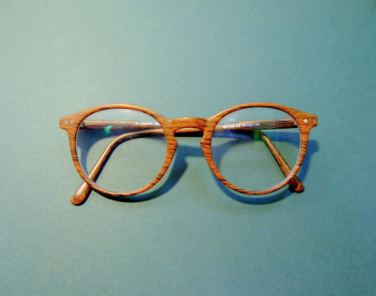 hero-img-02 Close-up of fashionable wooden frame eyeglasses on a solid blue background.